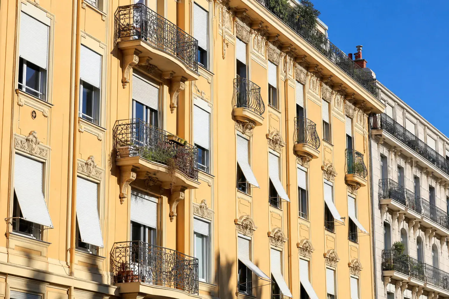 Façade d’immeuble niçois aux volets roulants, fenêtres en pleine lumière